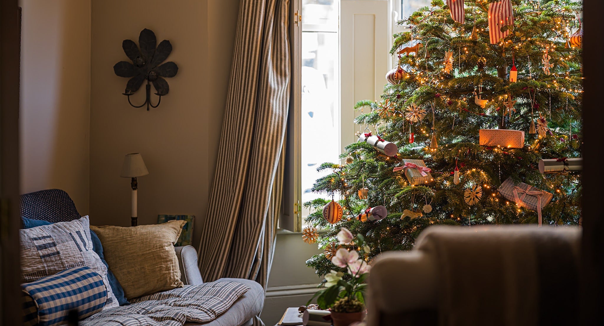 a christmas tree lit up and decorated, sitting in the living room by a cosy sofa