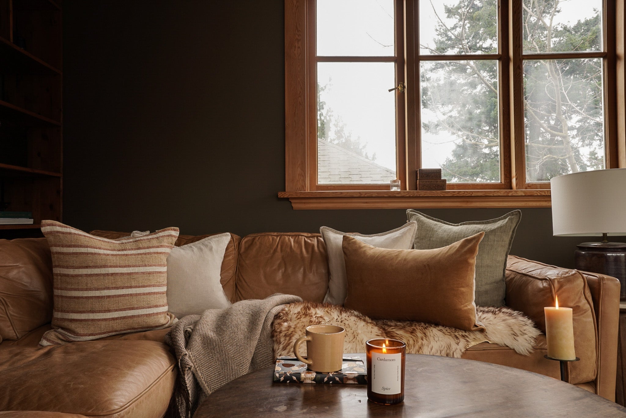 an inviting coach adorned with plump, velvet cushions and a cosy, warm, woollen blanket near a wintry windowscape 