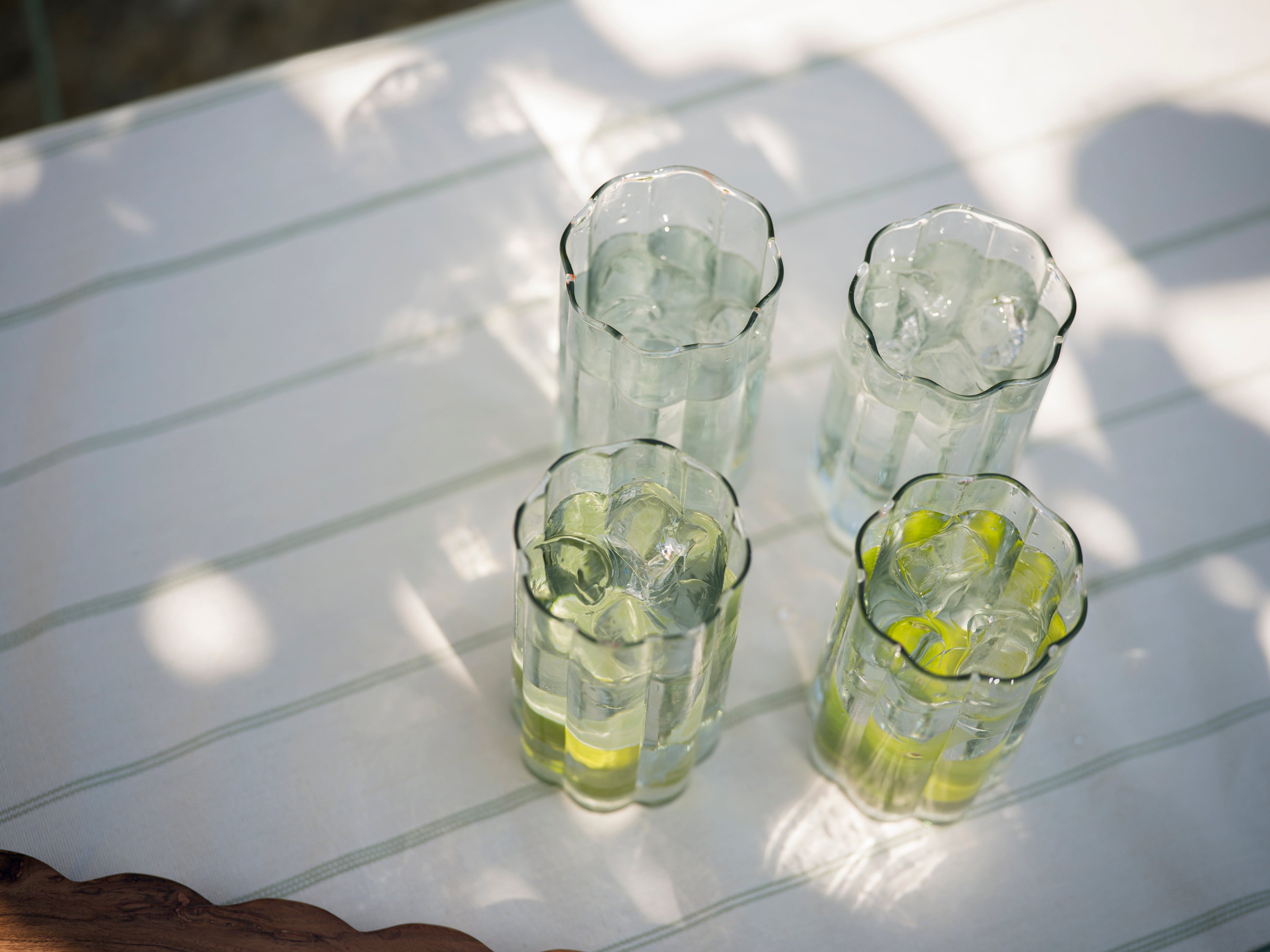 four beautiful scalloped glasses sit with lemon water on a striped cotton tablecloth in the sunshine