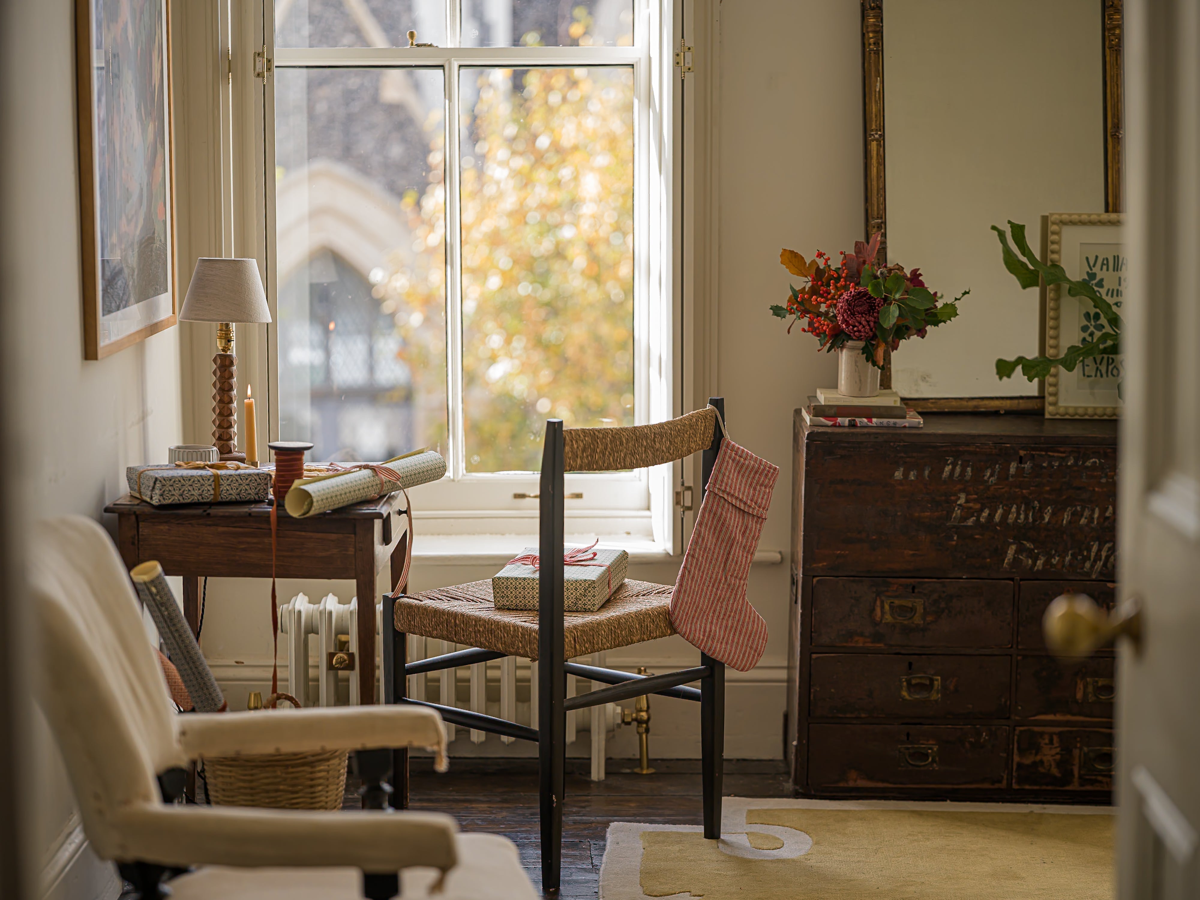 A large windowsill, outside of which you can faintly see an old fashioned church and late-autumnal foliage on the tree. Closer to the camera are beautiful wrapping supplies - ribbon, paper, tape, and presents.