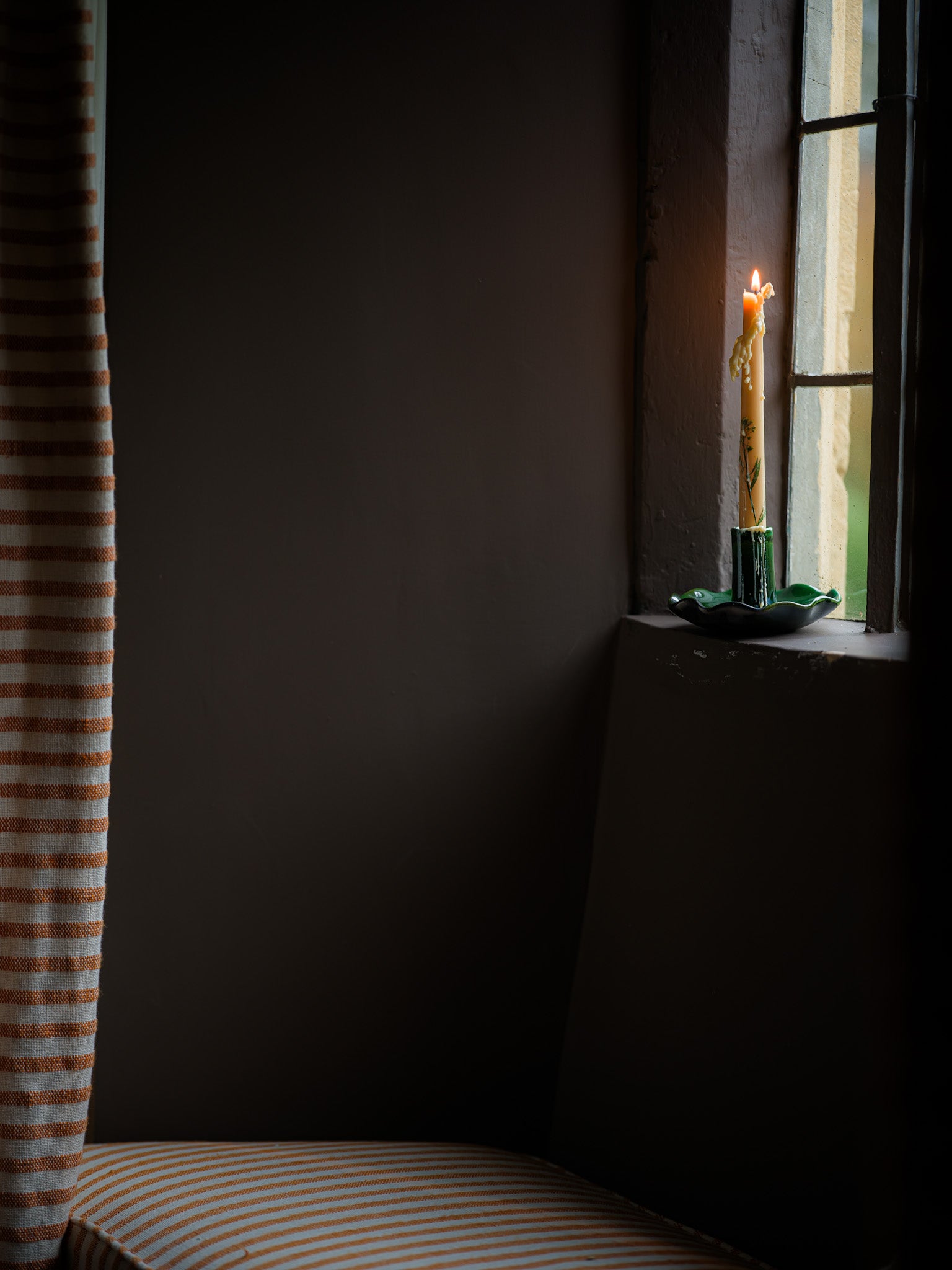 Candle in a window with striped curtain on a dark wall