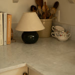 Ceramic pots with wooden spoons, books, and a lamp on a countertop.
