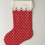 A red Christmas stocking with a repeating black and white floral pattern, a white fabric cuff with black stitched trim, and a white hanging loop, shown against a light gray background.