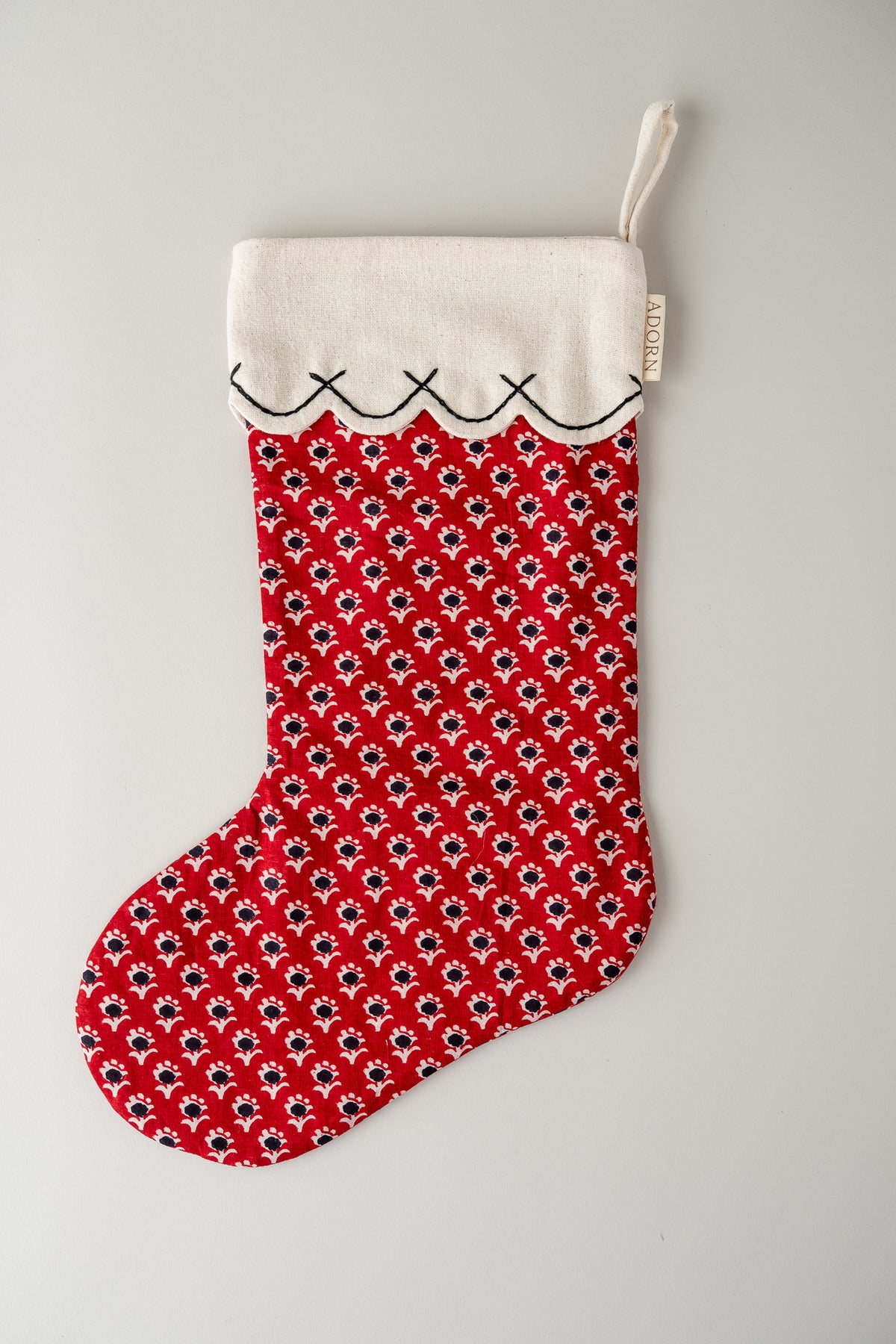 A red Christmas stocking with a repeating black and white floral pattern, a white fabric cuff with black stitched trim, and a white hanging loop, shown against a light gray background.
