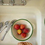 Green colander with peaches in a kitchen sink