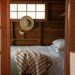 Bedroom with wooden walls, a bed with a striped blanket, and a hat on a shelf.