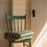 Green chair with a striped cushion against a white wall.