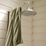 Outdoor shower with a green and white striped towel hanging on a metal rod.