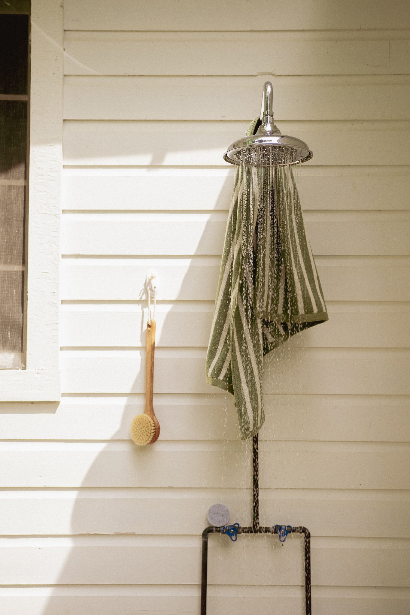 Outdoor shower setup with a showerhead, hose, and towel on a wooden wall.