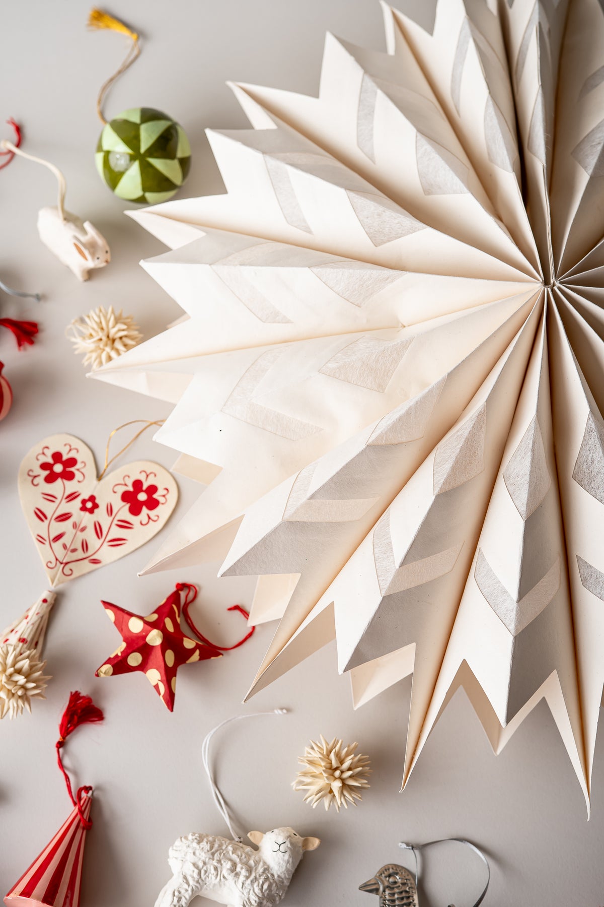 A large cream-colored paper fan decoration with a geometric zigzag pattern, displayed on a light gray surface alongside other festive ornaments and decorative items.