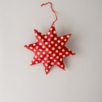A red fabric star-shaped hanging ornament with white polka dots and a red hanging string, photographed against a plain light gray background.