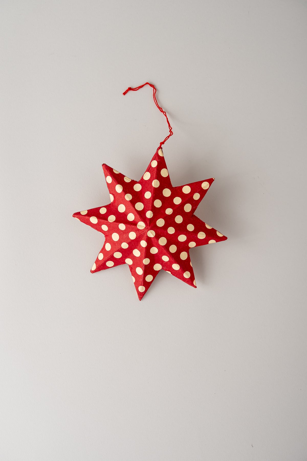 A red fabric star-shaped hanging ornament with white polka dots and a red hanging string, photographed against a plain light gray background.
