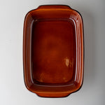 An amber-brown rectangular ceramic baking dish with rounded corners and small integrated handles, shown from a top-down perspective on a light gray background.