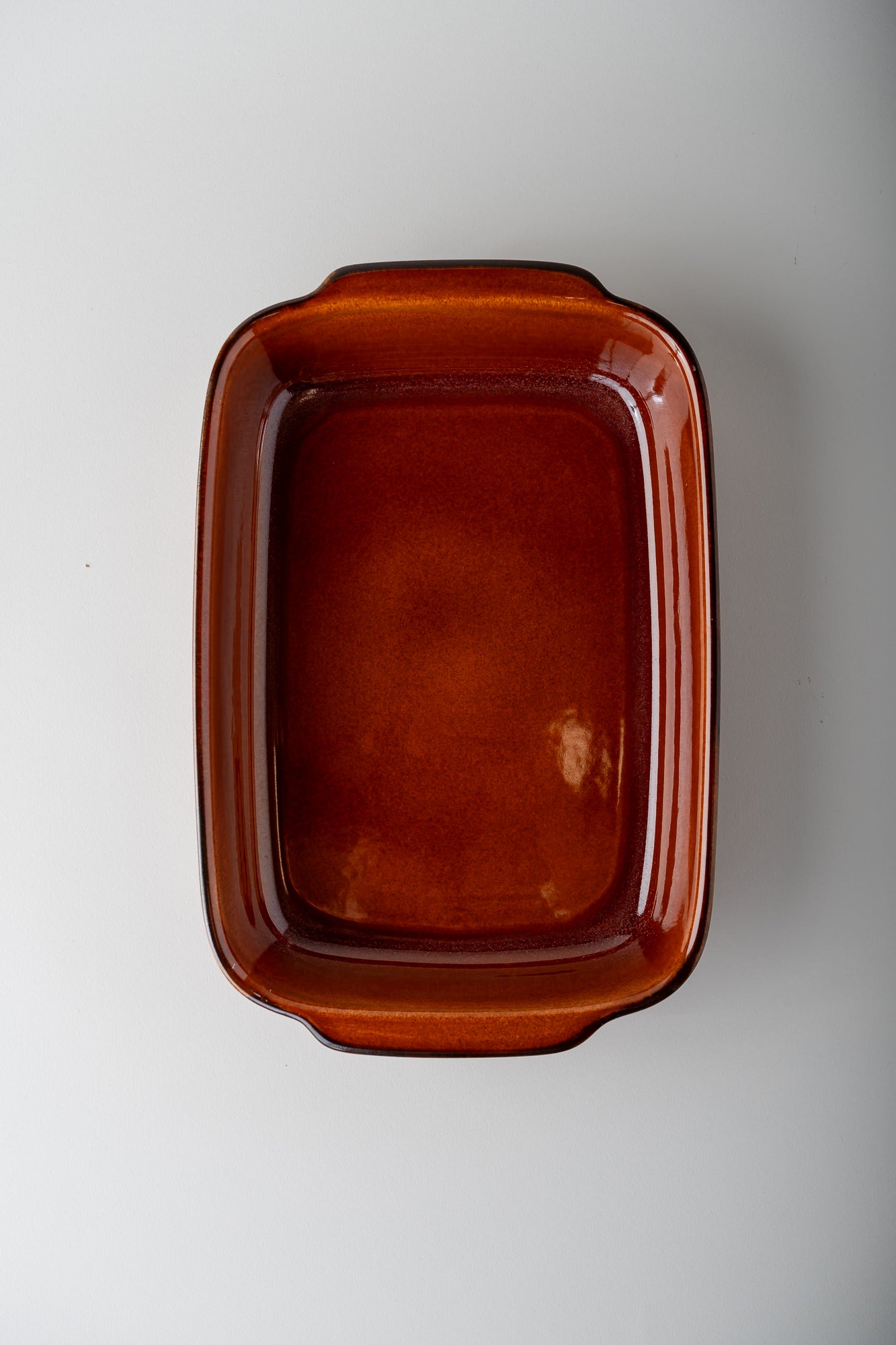 An amber-brown rectangular ceramic baking dish with rounded corners and small integrated handles, shown from a top-down perspective on a light gray background.