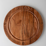 A round wooden cutting board with engraved leaf patterns around the edge and the word 'BREAD' embossed at the top, shown on a light gray background.