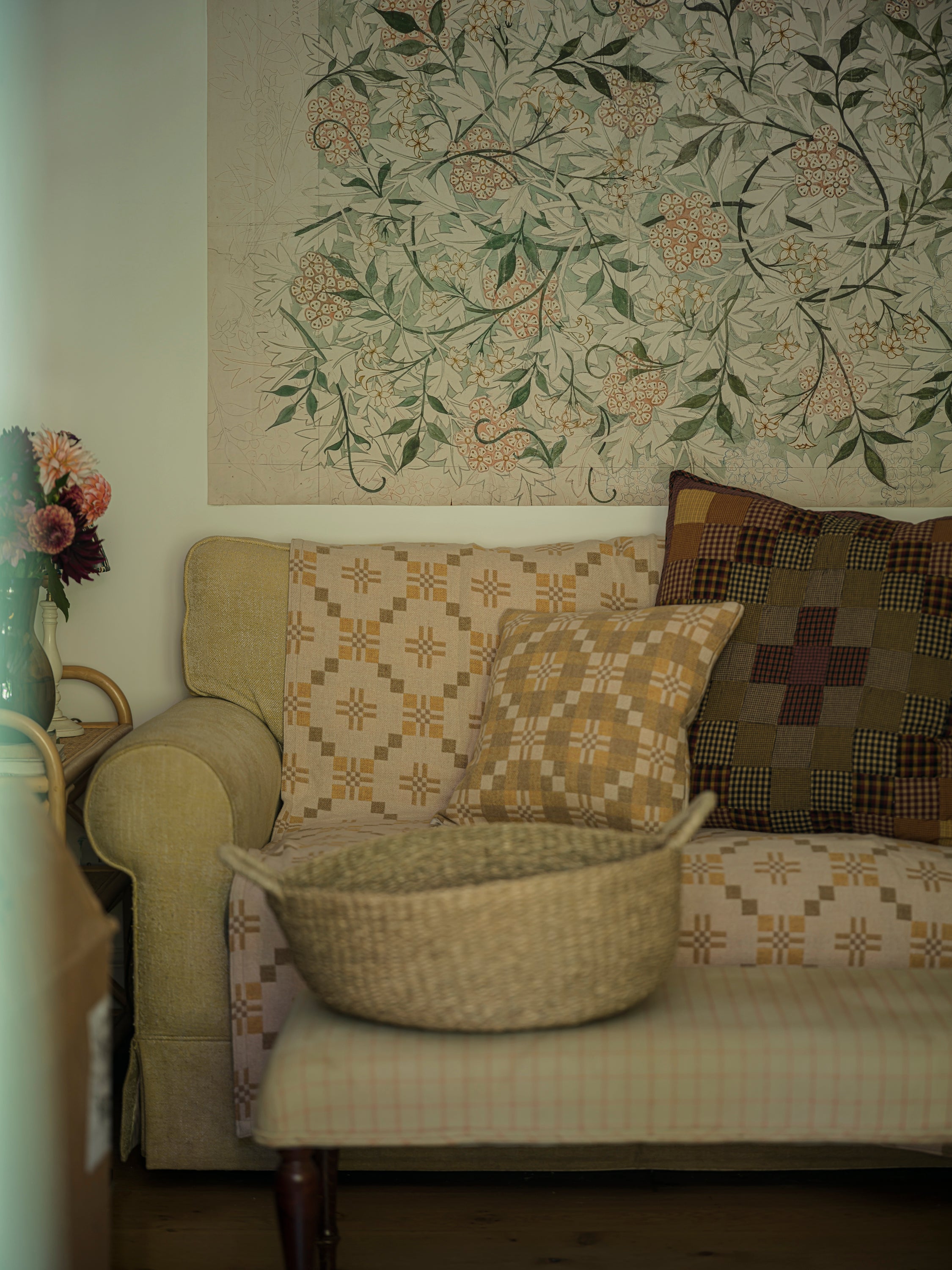 Patterned sofa with a woven basket and decorative pillows against a floral wall tapestry.