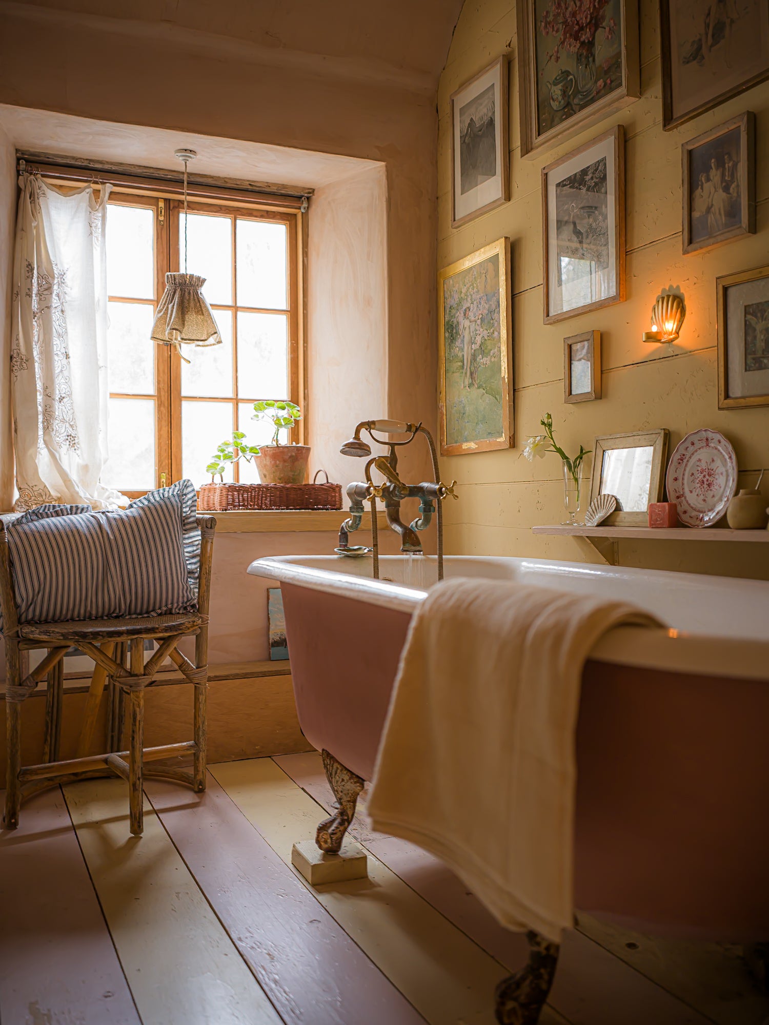 Vintage-style bathroom with clawfoot bathtub, wooden floor, and framed pictures on the wall.
