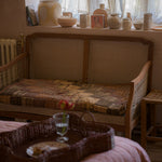Wicker bench with patchwork cushion in a room with curtains and decorative items.