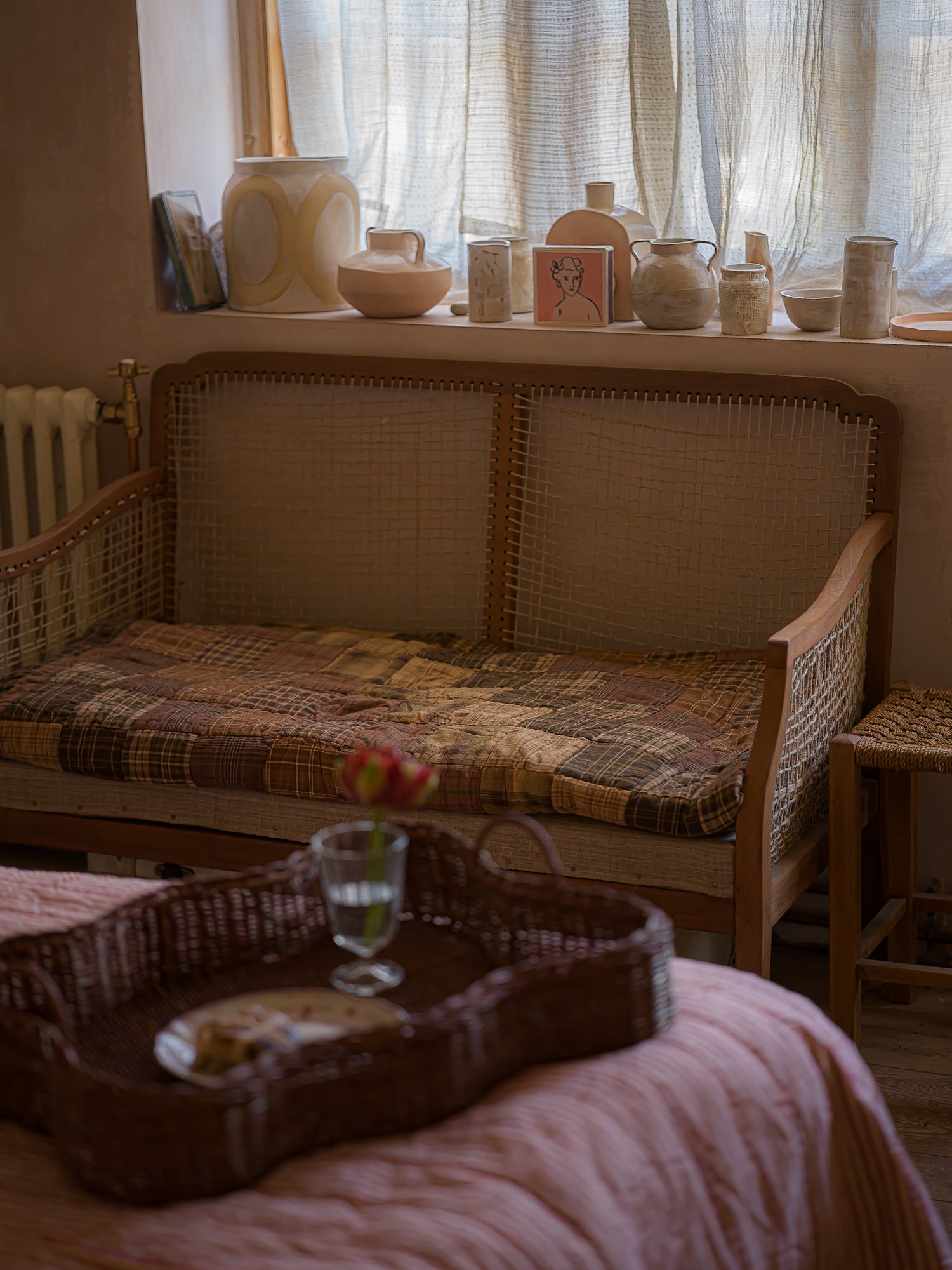 Wicker bench with patchwork cushion in a room with curtains and decorative items.