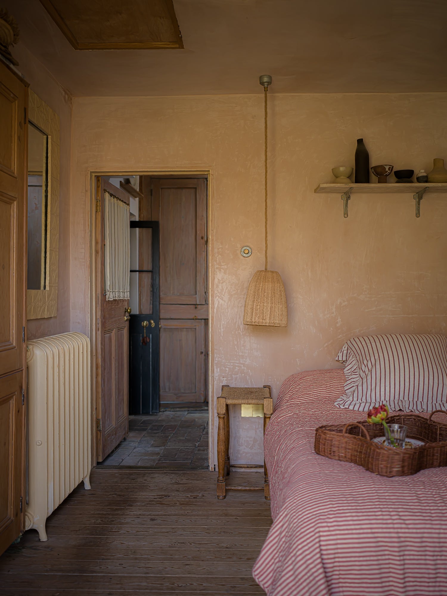 Bedroom with pink striped bedspread, wooden nightstand, and open door leading to another room.