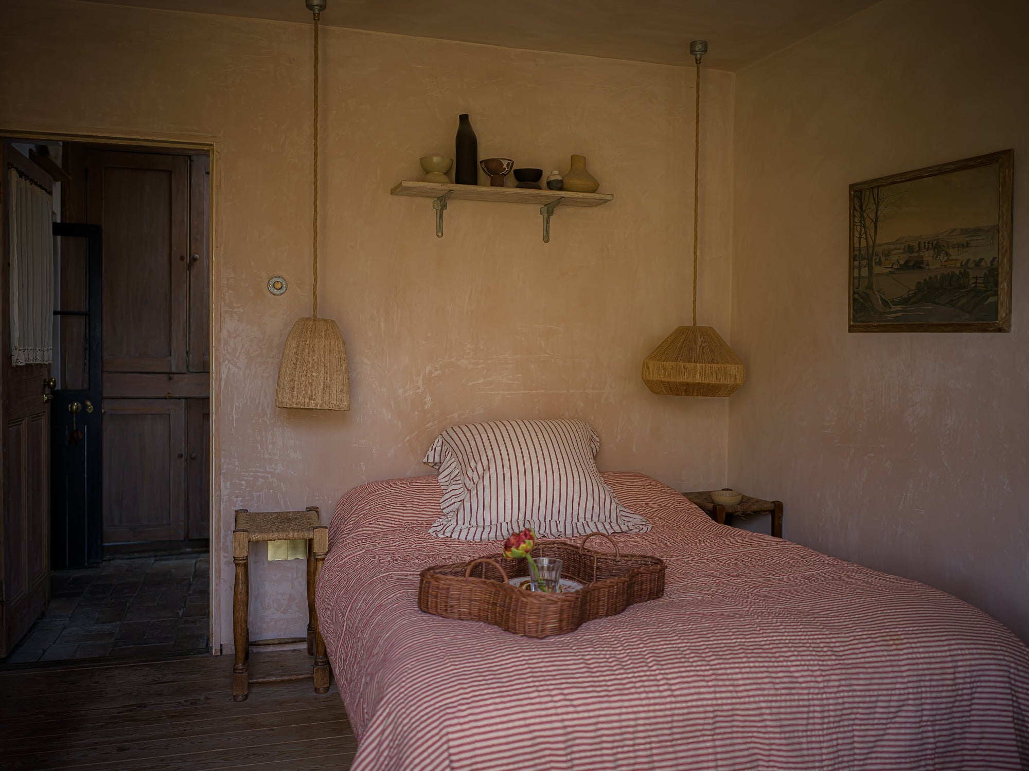 Bedroom with pink striped bedspread, wooden nightstands, and a shelf on the wall.
