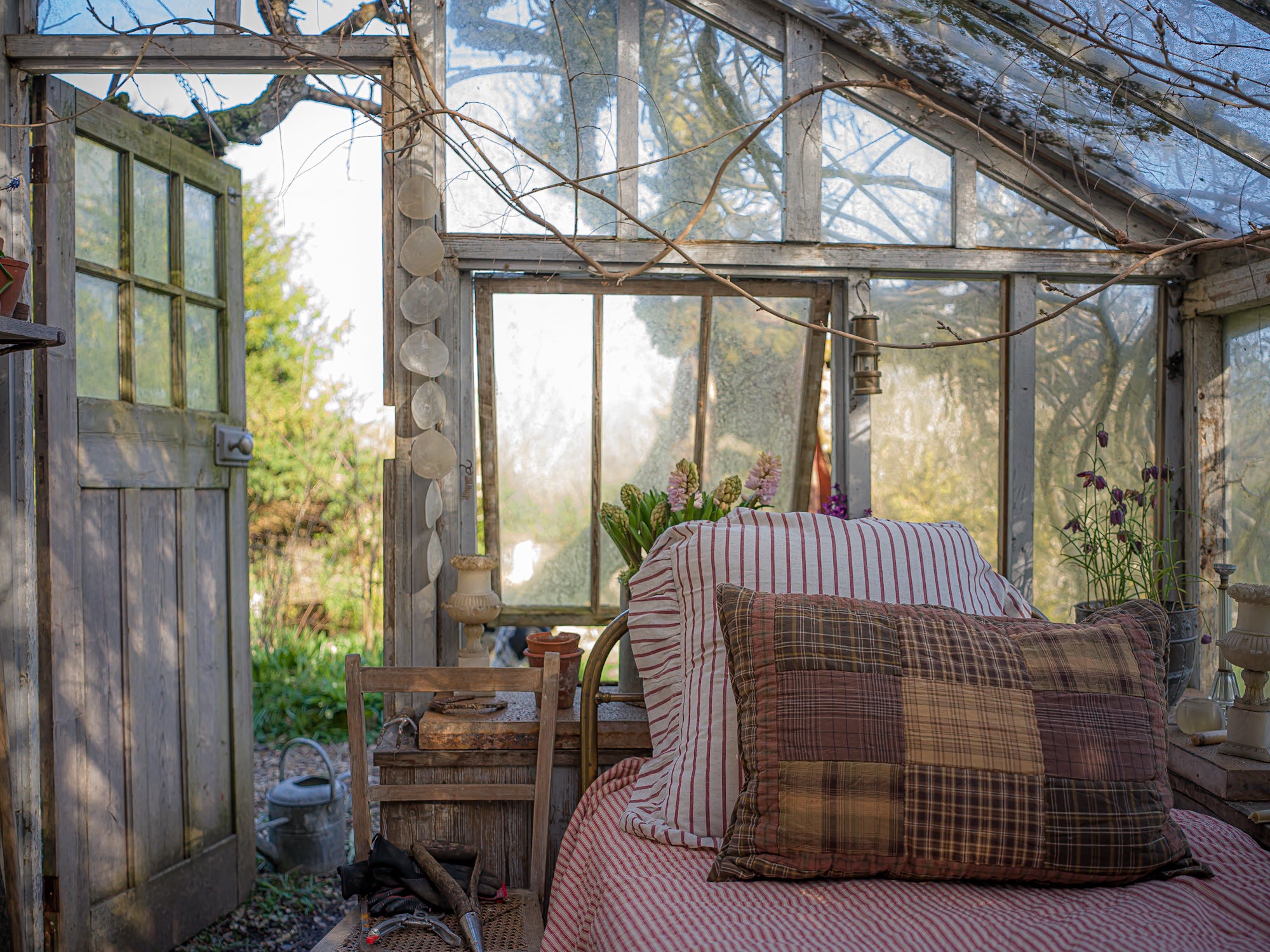 Cozy interior of a greenhouse with a bed, pillows, and a wooden chair.