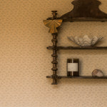 A dark brown wooden wall-mounted shelf with three tiers, styled with home decor items including a gold fan, a white seashell bowl, a candle, and another shell, set against a textured beige wallpaper background.