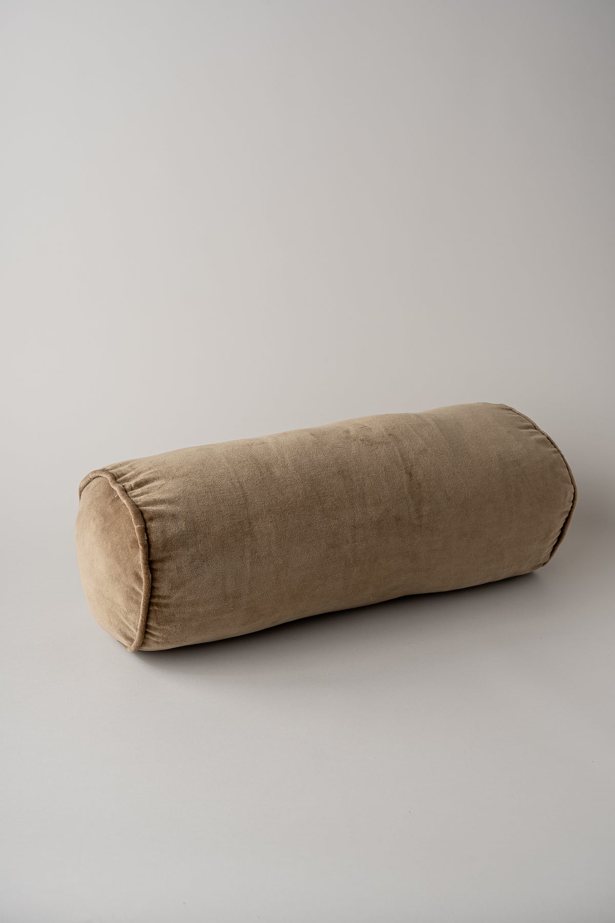 A cylindrical bolster pillow in a textured taupe fabric, photographed on a neutral light gray background.